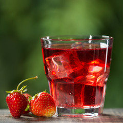 a refreshing summer drink with strawberries and ice cubes, next to a glass are the fruits of strawberries