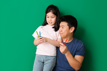 Happy Asian man and his little daughter with markers on color background