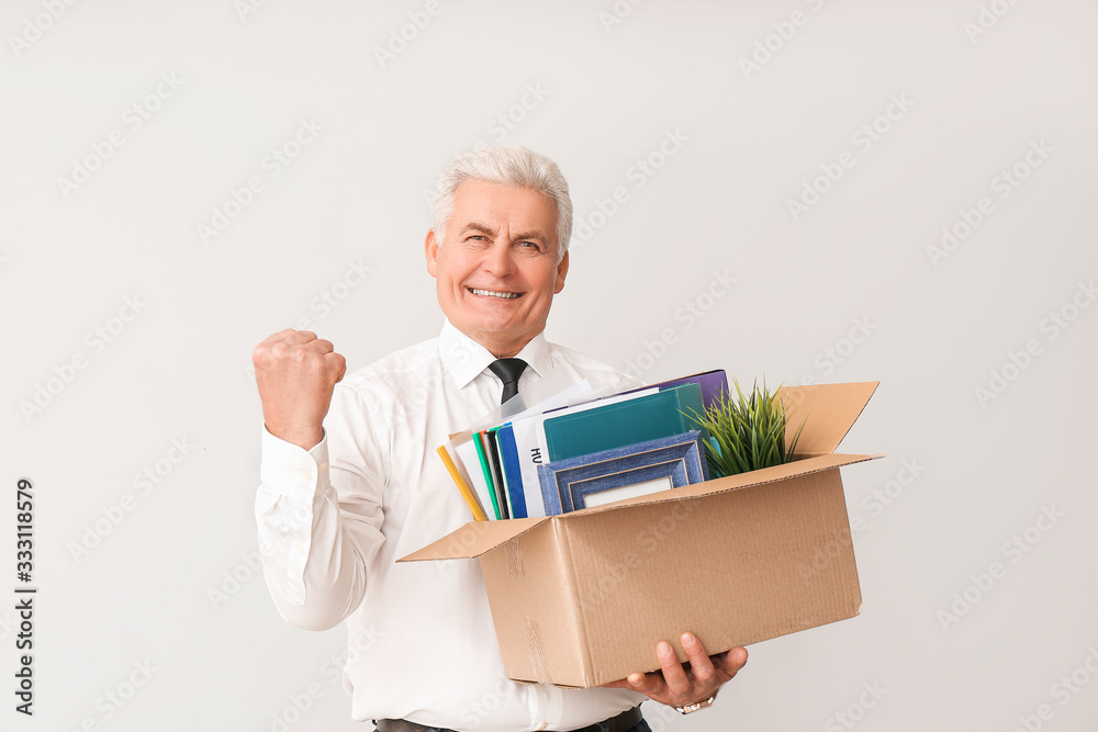 Happy fired mature man with personal stuff on light background