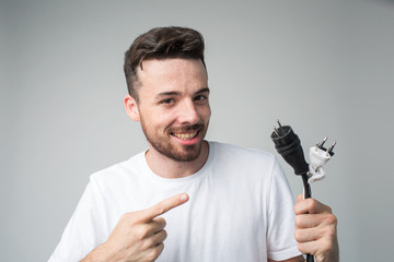 Young man isolated over background. Guy repair master hold cord with socket in hand and point on it. Happy cheerful positive master want to use it.