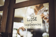 Store owner turning close sign broad through the door glass for social distancing prevent corona virus outbreak.