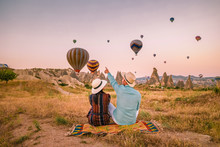 Cappadocia Turkey During Sunrise, Couple Mid Age Men And Woman On Vacation In The Hills Of Goreme Capadocia Turkey, Men And Woman Looking Sunrsise With Hot Air Balloons In Cappadocia