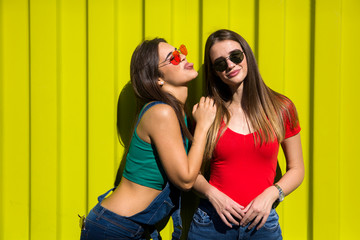 Two cute casual young women fooling around in front of yellow wall