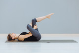 Relaxing back pain exercise concept. Attractive sportive woman doing pilates exercise lying on yoga mat at empty room at grey wall ackground.