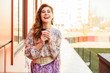 © Вячеслав Чичаев - Photo in bright weather of a fashionable glamorous beautiful woman with long hair against the background of the spring city in the sun. Model is standing outdoors with a cup of coffee in her hands.