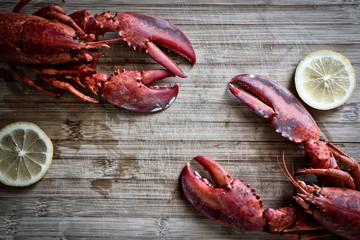 Steamed red lobsters with lemon, seafood utensils on the rustic wooden table. Maine lobsters. Two boiled lobsters.