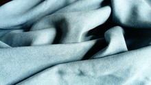 Dense Velvety Fabric For Curtains Of The Color Of Sea Wave, Randomly Folded By Beautiful Smooth Waves With A Play Of Light And Shadow. Daylight On Blue And Gray Textile.