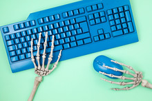 Human Skeleton Hands Typing On Blue Computer Keyboard, Flat Lay, Top View. Social Media Victim, Self Isolation, Internet Addiction