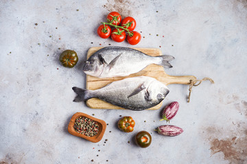 Fish dishes cooking preparation with dorado in backing form in shape of fish with healthy vegetables on gray background with ingredients, top view