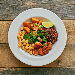 Wall Mural - Buddha nourish bowl with garlic grilled shrimps, baked sweet potato, black quinoa, chickpeas, humus and lime on a table. Top view, directly above.