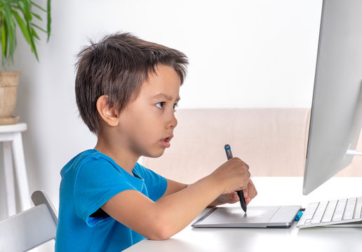 Little boy browses the internrt on a  desktop computer with graphics tablet. Modern lifestyle.