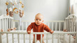 Beautiful little girl in a crib in a cozy light room in a sweater of fashionable shades. learns to stand at the support. cheerful little girl standing in the crib at home