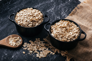 Two black bowls and spoon with raw oatmeal on a black background. Breakfast with fibers for a balanced diet. Oat photo