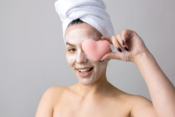 Beauty portrait of woman in white towel on head  with a sponge for a body in view of a pink heart. Skincare cleansing eco organic cosmetic spa relax concept.