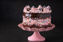 Trendy Sprinkle Fault Line Cake With Chocolate Ganache And Pink Color Decor On A Cake Stand, Dark Background With Copy Space.