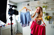 © artiemedvedev - Fashion blogger woman in jeans and turtleneck showing casual colorful shirts on camera. Stylist influencer girl showing trendy clothes filming vlog episode for her channel. Opinion leader sets trends.