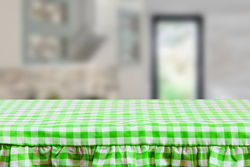 Empty wooden desk table with green checkered tablecloth over abstract blurred kitchen background. Template for your food and product display montage.