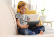 © New Africa - Cute little boy with headphones and tablet listening to audiobook at home