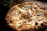 Pizza z gruszką, orzechami i kozim serem na drewnianym, naturalnym, brązowym stole. Obok rozmaryn w doniczce