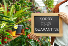 Business Owner Holding Sign With Text SORRY WE ARE CLOSED QUARANTINE In Flower Shop, Closeup