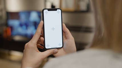 Young woman at modern room using smartphone or mobile phone with green white screen chroma key with track points watching content videos blogs Close up view TV on background