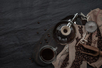 Cup of coffee and coffee beans roating with old wooden scoop and coffee beans around on the wooden and dark stone background. Top view with copy space for your text.