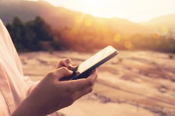 Wall Mural - Woman hand using smart phone on top of mountain with sunset sky abstract background.