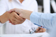 © H_Ko - Partnership agreement closeup with man in suit shake hand as hello in background. Friend welcome mediation offer greet gesture participate approval motivation strike arm bargain concept