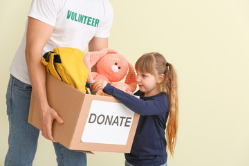 Wall Mural - Volunteer with donations for orphans and little child on color background