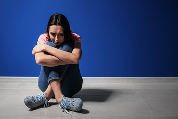 Wall Mural - Depressed young woman sitting near color wall