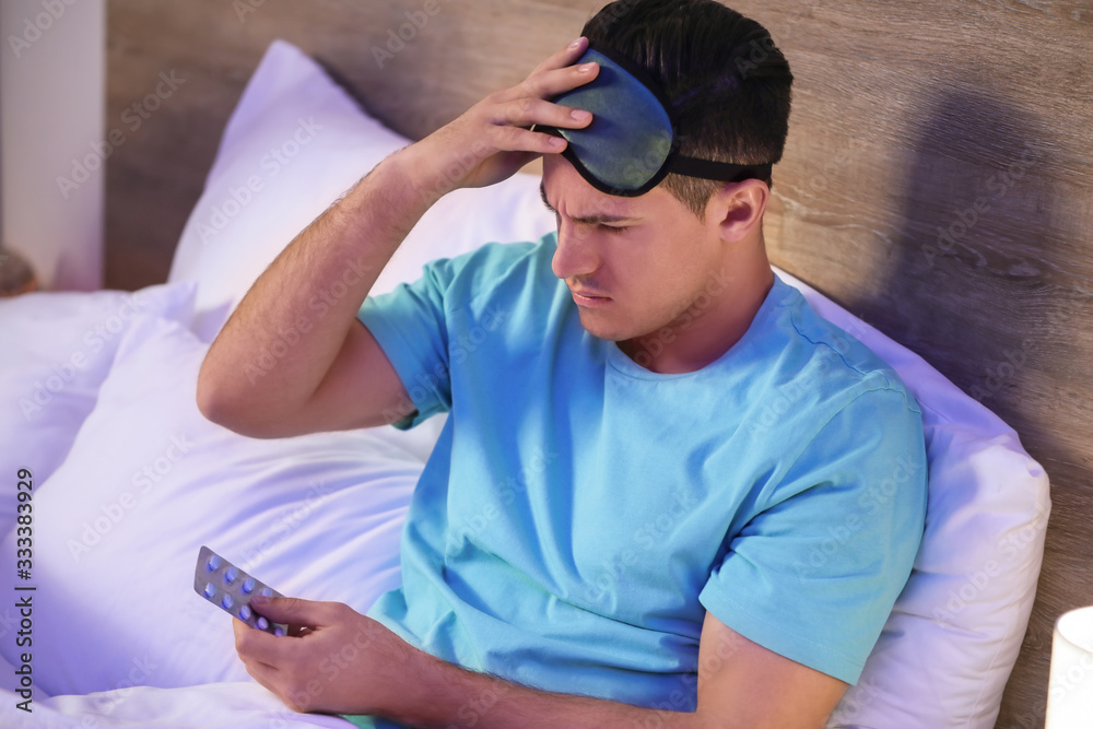 Tired man with pills for insomnia in bedroom