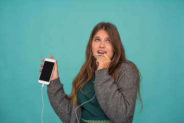 Wall Mural - Fashion pretty sweet carefree teenage girl listening music in headphones, singing and talking with smartphone over blue background