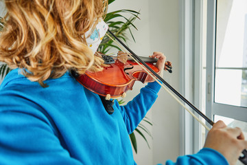 Life in quarantine coronavirus: games and activities for the kids at home during quarantine covid-19. A teenage girl in a mask makes music playing the violin. Selective focus.