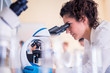 © Vladimir Borovic - Young female scientist looking through a microscope in a laboratory doing research on finding medicine pharmacy cure vaccine