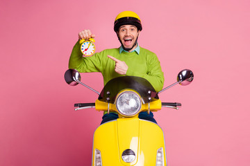 Wall Mural - Portrait of his he nice attractive glad cheerful cheery guy sitting on moped holding in hand demonstrating recommending funny alarm clock isolated over pink pastel color background