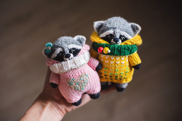 Handmade knitted toys. Amigurumi raccoon toys in yellow sweater and pink overalls. Crochet stuffed animals. 