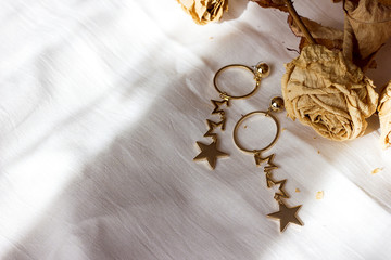 Beautiful pendant earrings gold and dried roses on a white bed, contrasting shades of cream-beige colors, space fir text