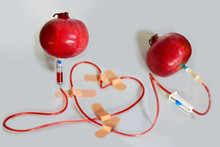 Two Pomegranates Connected By A Medical Dropper Iv Cannula With A Pomegranate Juice, Shaped In A Heart Form, Fixed By Patches