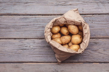 Wall Mural - A paper bag full of fresh homegrown potatoes on a wooden background