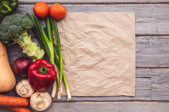 Top view of various fresh organic vegetables with a blank brown paper bag