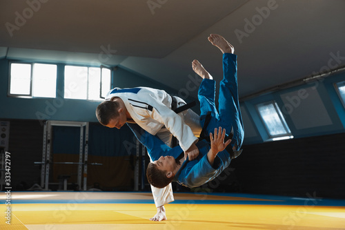 Dekoracja na wymiar  dwoch-mlodych-kaukaskich-wojownikow-judo-w-bialo-niebieskim-kimonie-z-czarnymi-pasami-trenuje-walki