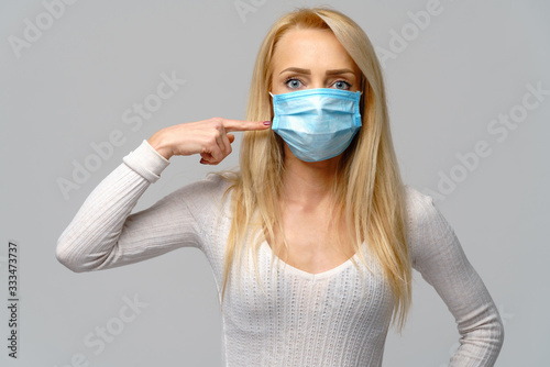 Studio portrait of young woman wearing a face protective mask isolated on gray background - flu virus epidemic protection, dust or pollen allergy, air pollution
