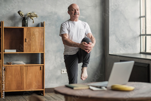 Fotomural man doing yoga exercise at home using online lesson on notebook.