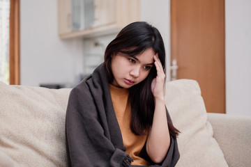 Wall Mural - Portrait of Young woman sitting on a couch, holding her head, having a strong headache. Pandemic 2019 Coronavirus 2019-nCoV Concept.