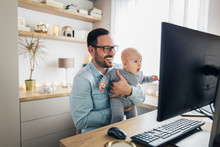 Young Father Working From Home And Holding His Baby Boy.