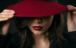 Close-up of sensual glamorous beauty hiding face under hat touching maroon wide brim with both hands