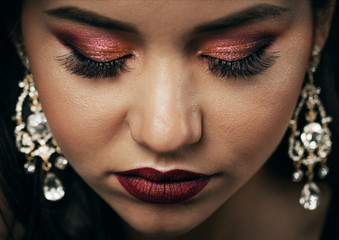 Close-up top view of elegant young woman face with rich make-up and jewel earrings, closed eyes