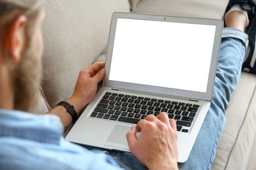 Young male tech user relaxing on sofa holding laptop computer mock up blank white screen. Man using modern notebook surfing internet, read news, distance online study work concept. Over shoulder view