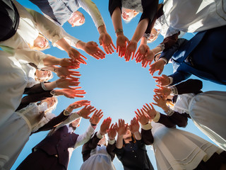 Students graduates make the shape of a circle from the palms of their hands.