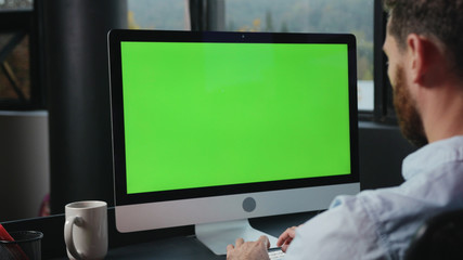 Mock-up chrome key green computer monitor on office table. Close-up manager working by personal computer in modern company.